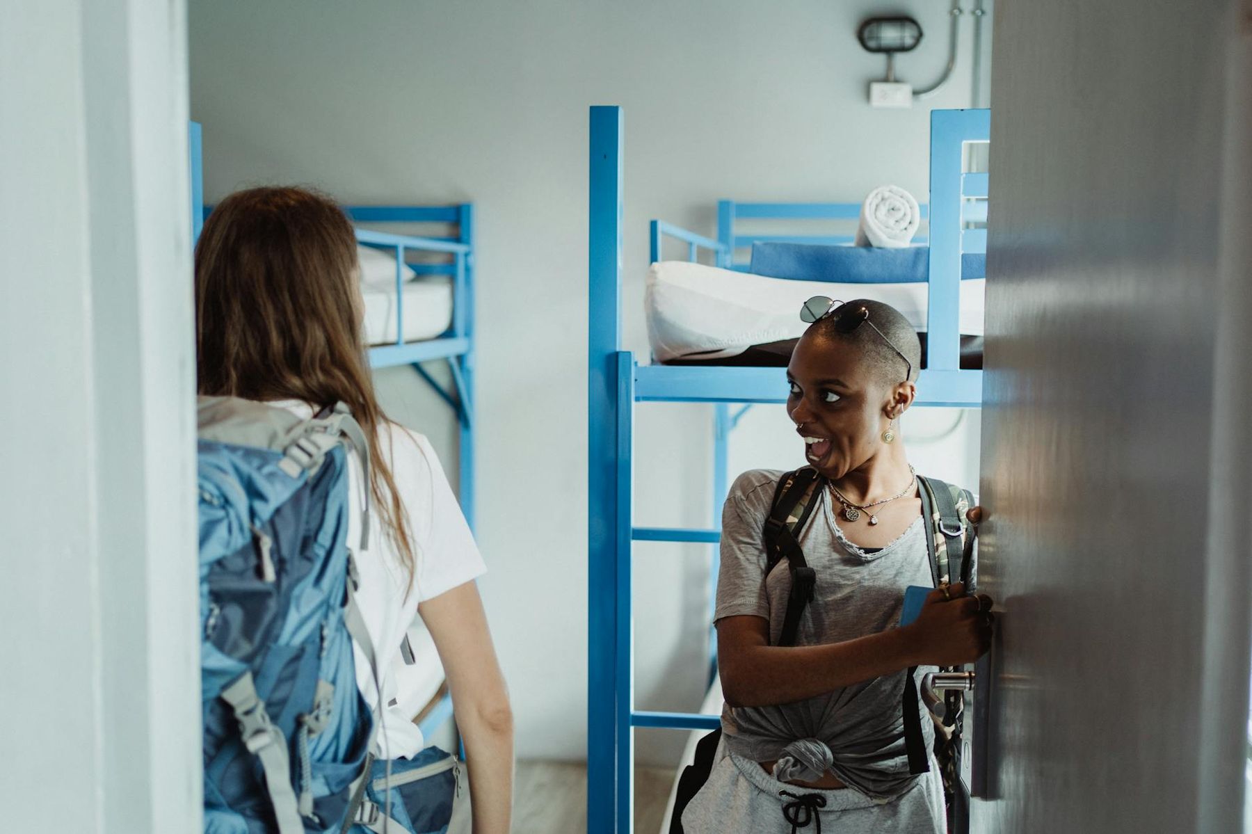 Two backpackers walking into an Auckland hostel dormitory with bunk beds